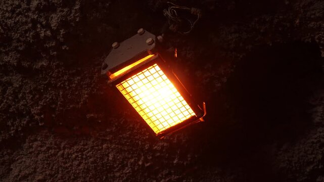 An orange infrared heater with a metal grille glows on a rough tunnel wall, providing warmth and light in a dark underground space.
