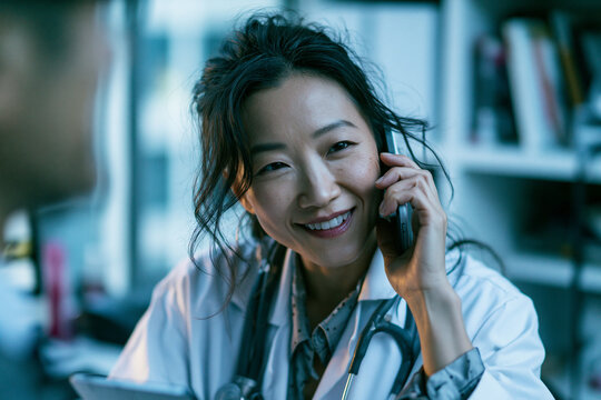 Asian Female Doctor Smiling While Talking on Phone