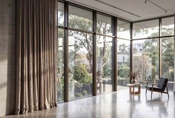 Fototapeta premium Minimalist contemporary interior with expansive floor-to-ceiling windows, neutral curtains, polished flooring and a comfortable lounge chair overlooking greenery.