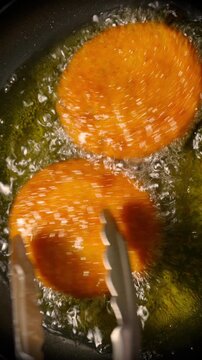 Breaded Patties Frying in Hot Oil. Close-up of golden breaded patties sizzling in bubbling oil while metal tongs turn them.