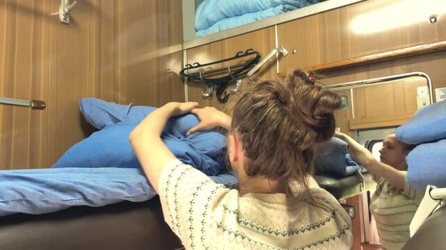 Young woman rolling up bedding inside a train compartment, passenger travel, sleeper carriage routine, rail journey, practical travel activity.