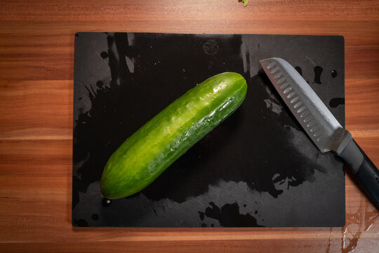 Fresh Whole Cucumber and Knife on Wet Cutting Board