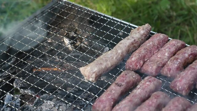 Male hand places cevapi on a charcoal grill with rising smoke outdoors. Traditional barbecue footage fits food, travel, summer and hospitality themes