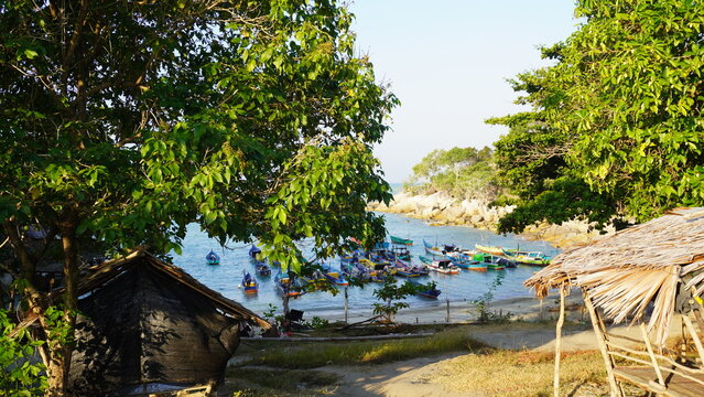 Colorful wooden fishing boats anchored in a calm coastal cove framed by lush green trees and traditional thatched-roof huts.