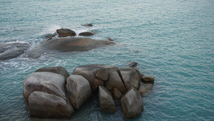 Fototapeta premium High angle view of large granite boulders sitting in turquoise sea water with small waves breaking.