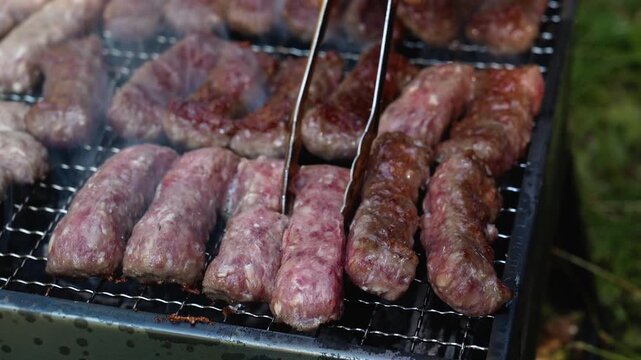 Tongs turn cevapi on a smoky charcoal grill during outdoor cooking. Traditional barbecue footage fits food, travel, summer and hospitality themes