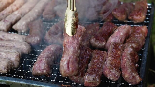 Tongs turn cevapi on a smoky charcoal grill during outdoor cooking. Traditional barbecue footage fits food, travel, summer and hospitality themes