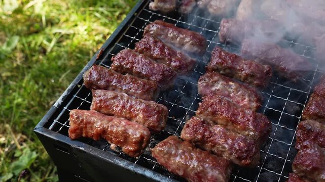 Cevapi cook on a hot charcoal grill as thick smoke rises outdoors. Traditional Balkan barbecue footage fits food, travel, summer and hospitality themes