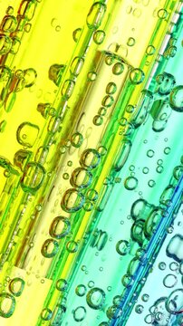 Colorful Liquid Bubbles in Transparent Tubes. Macro view of numerous air bubbles moving through yellow, and green liquid inside parallel transparent tubes.