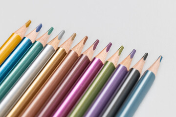 Fototapeta premium Macro close up of metallic colored pencils arranged diagonally in a row on white background with copy space