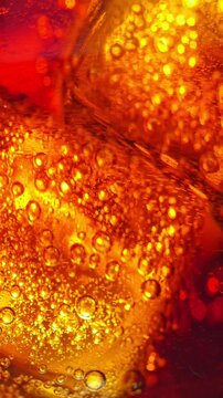 Ice Cubes in Cola Close-Up. Macro view of translucent ice cubes surrounded by bubbles in a glowing amber carbonated drink.