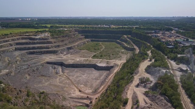 Aerial footage shows large open pit mine with stone crushing processing facility, conveyor belts, railway track, and deep terraced excavation area under hazy sky.