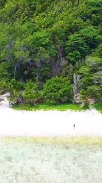 Vertical aerial tracking shot flying parallel to Anse Fourmis beach in Seychelles with turquoise sea, tropical vegetation and scenic coastal landscape.