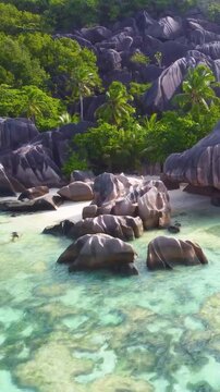 Vertical aerial pull back view revealing Anse Source d'Argent in Seychelles with turquoise water, granite rocks, white sand and tropical coastal scenery.