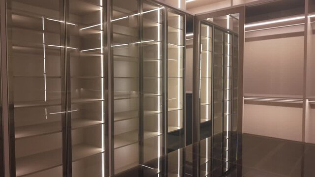 Modern luxury walk-in closet with integrated LED strip lighting, dark wood island, and tufted ottoman bench.