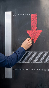 Hand drawing a red arrow pointing down on a chalkboard, representing a downward trend or decline, suitable for financial or business concepts