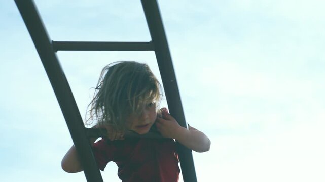 Boy climbing a metal ladder at the playground filmed from directly below looking up through the rungs