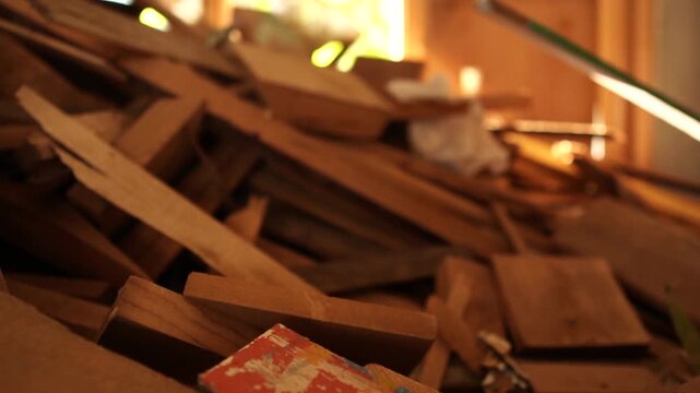 Cinematic close up dolly in shot with a rack focus from a pile of discarded wood scraps toward a sunlit window.