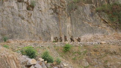 Naklejka premium A military squad in camouflage takes a tactical position with rifles during a mission on a rugged cliffside, demonstrating teamwork and battlefield vigilance.
