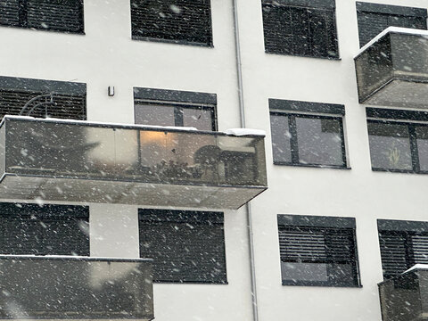 Snow falls and covers modern apartment building with open balconies and windows