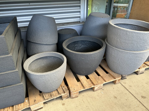 Different types of gray planters sit on a wooden pallet outside a store