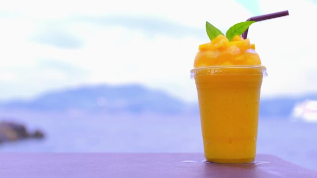 Smoothie made from fresh mango fruits against the backdrop of a seascape. Fruit and yoghurt ice cream decorated with leaves. Glass of tropical dessert close-up.