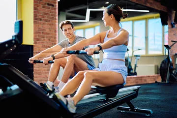 Fotobehang Sportschool Young man and woman exercising together on rowing machines, focusing on fitness and a healthy lifestyle in a modern gym  © we.bond.creations