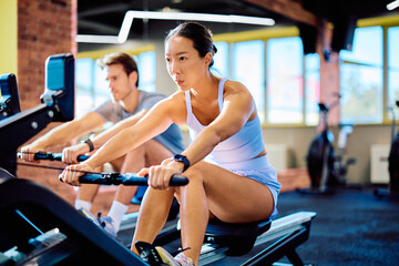 People working out in a gym, pulling handles of stationary rowers during an intense fitness exercise for health and wellness © we.bond.creations