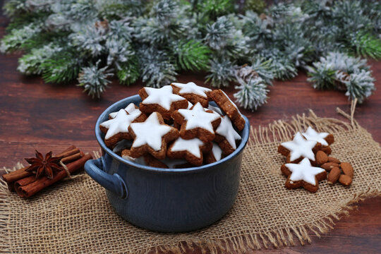 Traditionelle Weihnachtspl&auml;tzchen. Zimtsterne f&uuml;r die Adventszeit, serviert in einer Keramikschale auf einer Jutematte zusammen mit Zimtstangen, Sternanis und Tannenzweigen.