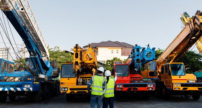 Inspecting a crane for preventive maintenance, two engineers in hard hats stand together while one points at heavy machinery