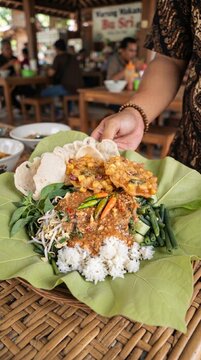 Traditional Indonesian Nasi Pecel Served on Fresh Green Leaves with Crispy Fried Tempeh