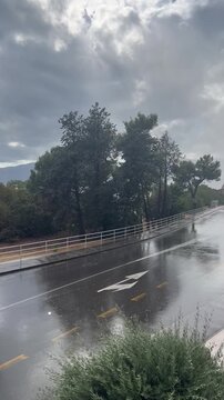 Rainy urban road in a Mediterranean setting, filmed during a heavy rain shower. Rainy day atmosphere and wet road reflections