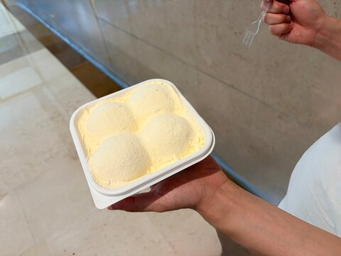 Hand Holding Container of Yellow Ice Cream Scoops Indoors