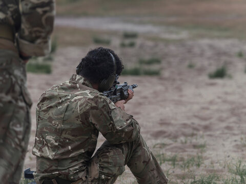 A young soldier fires an SA80 rifle from the kneeling position while an instructor stands alongside during weapon handling training.