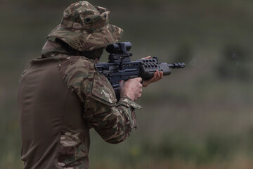 A soldier in a wide brimmed bush hat fires his service rifle from the standing position, muzzle smoke drifting into soft green bokeh. © Victor