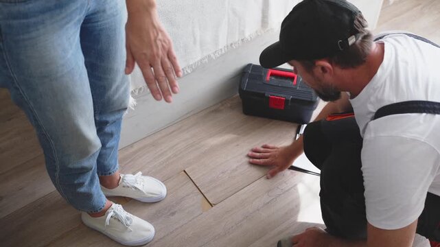 Professional contractor inspecting and measuring damaged laminate flooring while documenting findings on clipboard, with homeowner observing the assessment and repair planning process.