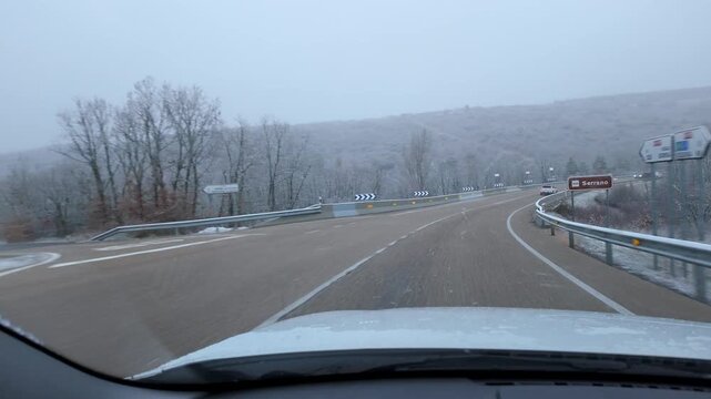 Driving toward a curved highway junction through snow covered woodland during winter snowfall