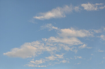 Fototapeta premium Clear blue sky with rare white clouds scattered across the sky. Sunlight and soft shadows from the clouds create a calm and peaceful atmosphere.