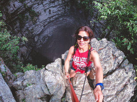 Woman smiles near dark water-filled cave entrance