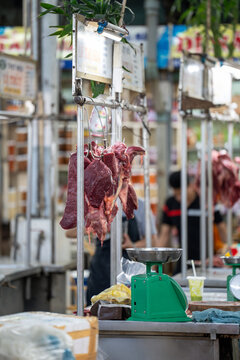 Fresh raw meat chops hanging on hooks at vendor stall at traditional wet street market department, chopped meat pieces selling at food marketplace in Asia, beef or pork produce wholesale at bazar.