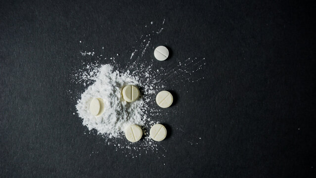 Top view of some white pills with powder form on black surface. Misused drugs concept. 