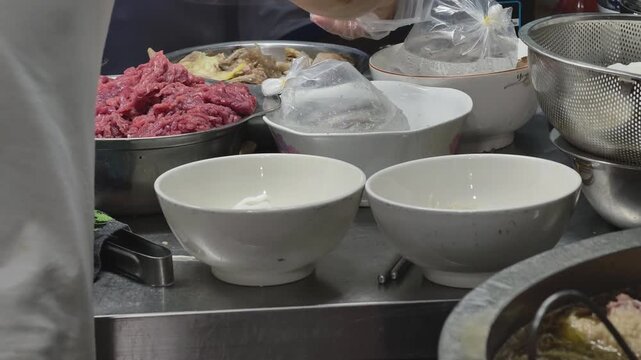 Preparation station at a traditional Vietnamese pho restaurant with raw beef, bowls, and boiling broth potv