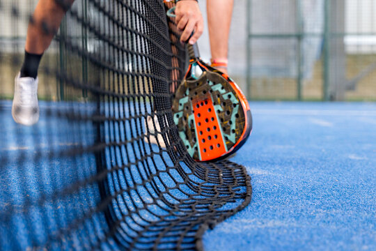 Padel player holding racket beside net on indoor court