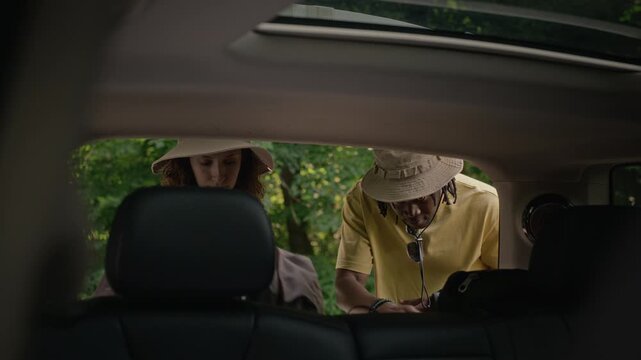 Multiethnic young adult friends taking backpacks out of car trunk before outdoor hike, then closing trunk door. Ideal for travel, adventure tourism, and active lifestyle marketing campaigns