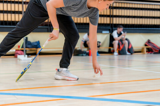 Female badminton player retrieves shuttlecock on indoor court