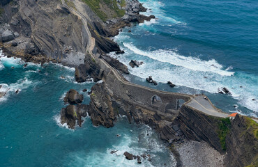 Fototapeta premium serene coastal pathway winding along rocky cliffs near the ocean with a concrete staircase leading to the shore, aerial perspective showcasing nature and architecture in harmony.