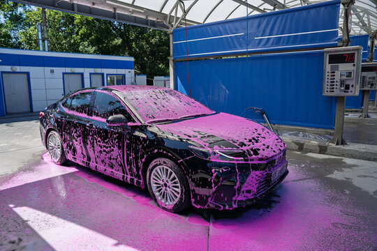 Black car covered in pink foam at a self-service car wash station