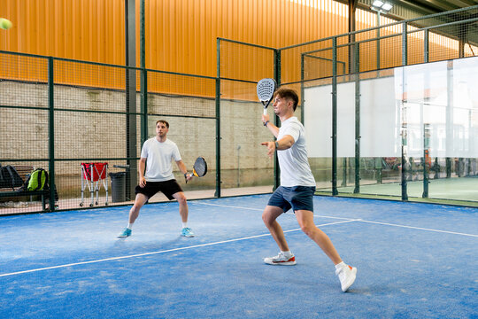 Two men play doubles padel match on indoor court