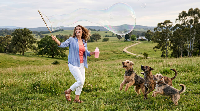 Woman blowing large bubbles in a grassy field with three dogs playing