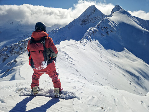 Snowboarder on alpine ridge above snowy mountain peaks